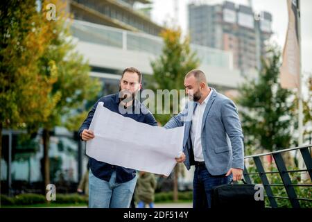 Two young engineers checking the architectural plan outdoors Stock Photo