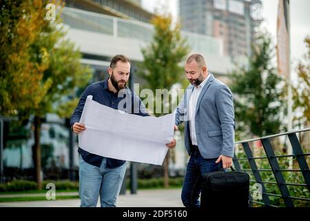Two young engineers checking the architectural plan outdoors Stock Photo