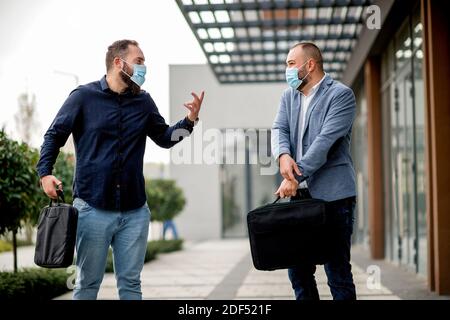 Two business colleagues in protective masks greeting each other outdoors near the office building Stock Photo