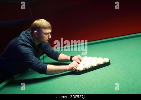 Man puts balls on billiard table at night Stock Photo