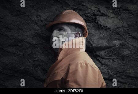 side view of rail worker with orange unifom and face mask in front of rock tunnel Stock Photo