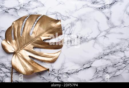 Golden monstera leaf on luxury marble background. Clean minimal flat lay design. Tropical gold foliage for trendy layout. Luxury fashion lifestyle con Stock Photo