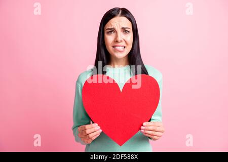 Photo portrait of woman biting lower lip holding big red heart postcard isolated on pastel pink colored background Stock Photo