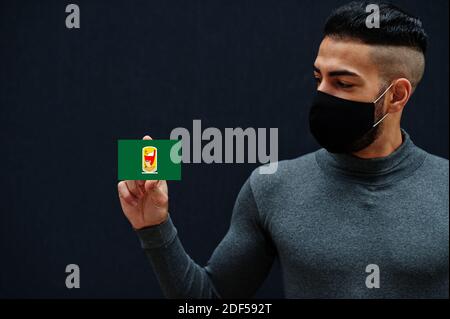 Egyptian man in gray turtleneck and black face protect mask show South Sinai flag isolated background. Governorates of Egypt coronavirus concept. Stock Photo