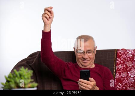 Senior man at home plays games on smartphone and rejoices at the victory. Home and spending time. Stock Photo
