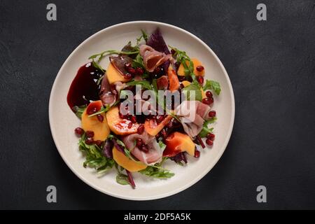 Salad with slices of bacon, persimmon, spinach, arugula, lettuce leaves  and pomegranate seeds and honey sauce Stock Photo