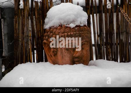 Old weathered terracotta buddha head covered with snow Stock Photo