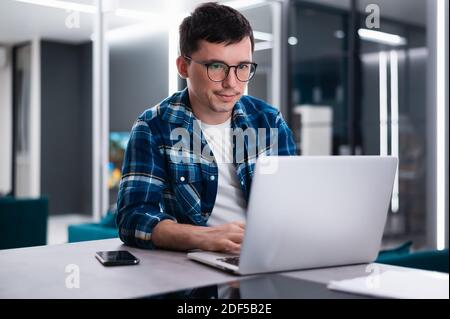 Focused young businessman study online watching webinar podcast on laptop listening learning education course conference calling make notes sit at wor Stock Photo