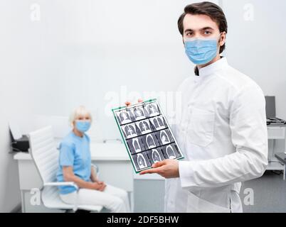 Pulmonologist wearing protective mask showing CT scan of lungs elderly patient. Complication after coronavirus disease in senior people, pneumonia Stock Photo