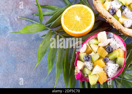 Exotic fruit salad served in half a dragon fruit and pineapple with palm leaf on stone background, copy space. Stock Photo