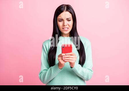 Photo portrait of scared woman biting lower lip holding phone with two hands isolated on pastel pink colored background Stock Photo