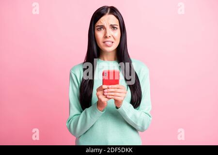 Photo portrait of guilty woman biting lower lip holding phone with two hands isolated on pastel pink colored background Stock Photo