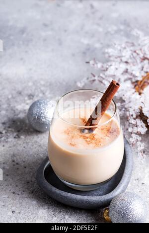 Winter spicy hot drink eggnog in a glass with cinamon in stone plate, ice frost branches on light stone table Stock Photo