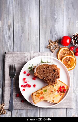 Christmas sliced chocolate cake and fruit cake with white icing and pomegranate kernels on plate with decoration on a wooden gray background, flat lay Stock Photo