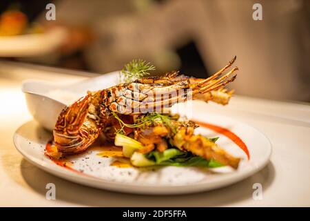 Fried cooked lobster on dinner, served gourmet luxury meal. Blurred chef and kitchen in the background Stock Photo