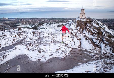 A fell runner runs through the snow on the summit of Arthur's Seat in Holyrood Park, Edinburgh. Stock Photo