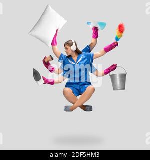 Music. Female housemaid in blue uniform multitask like shiva isolated on gray background. Young woman chambermaid with various items. Professional occupation, time concept. Copyspace for ad, design. Stock Photo