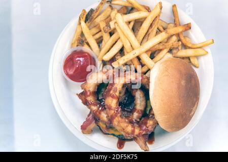 Overhead view of huge onion rings drizzled with barbecue sauce on hamburger served with french fries and dipping sauce. Stock Photo