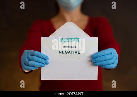 Woman Holding Negative Antigen Detection Test for Covid-19. Person Wearing Face Mask and Blue Surgical Gloves Showing Open Envelope with Negative Resu Stock Photo