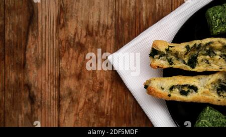 Rollini with brynza cheese and spinach on a black plate with a wooden background. Green squares of dried spinach on a plate Stock Photo