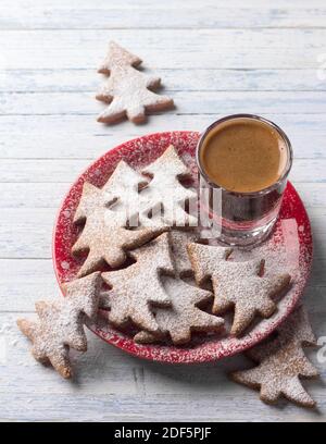 Oatmeal gingerbread cookies in the shape of Christmas tree on a red plate sprinkled with powdered sugar with a coffee shot  on a light blue background Stock Photo
