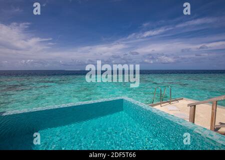 Luxurious beach resort with swimming pool and beach chairs or loungers under umbrellas with palm trees and blue sky. Summer travel and vacation scene Stock Photo