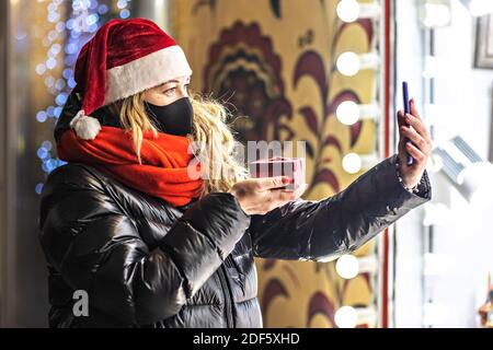 A woman with long hair in a Santa hat communicates on a smartphone via video communication. Congratulates relatives on Christmas and shows a gift. New Stock Photo