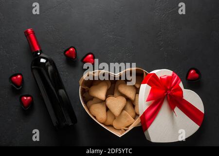 Bottle of red wine and heart cookies in gift on black. Valentine's Day Greeting card. View from above. Space for text. Stock Photo