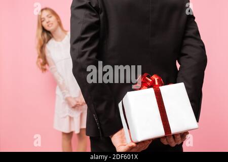 Elegant man in a suit makes a surprise to a woman, gives a bouquet of flowers and a box with a gift, on a pink background, concept of women's day Stock Photo