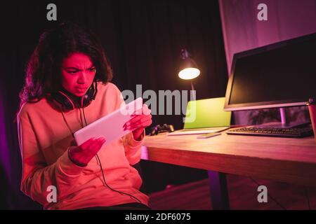 Concentrated african american gamer in headset using digital tablet near devices on blurred background Stock Photo