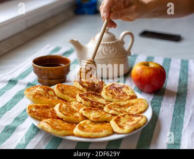 Woman pouring honey on ruddy homemade fritters. Honey dripping on tasty pancakes laid out on a plate. Selective focus Stock Photo