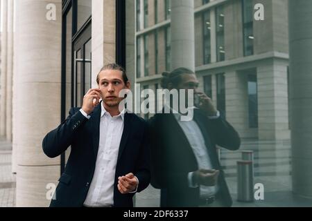 Businessman talking over smart phone while standing against modern building Stock Photo