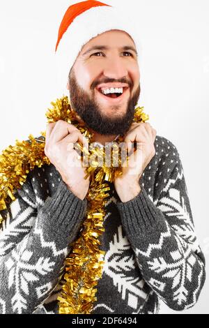 A handsome man with a beard, wearing a Santa Claus hat, rejoices and waits for the new year, on a white background. Stock Photo