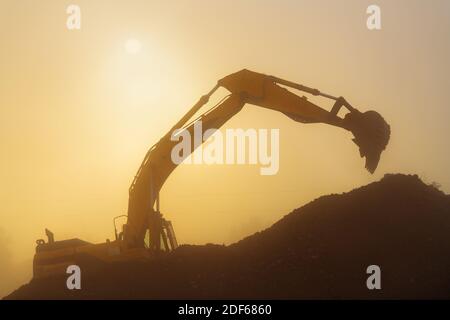 An excavator performs work in rubble in hazy and dusty early morning conditions. Stock Photo