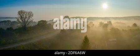 Panorama of scenic aerial view over cottage settlement, forest, landscape vegetation at sunrise in autumn fog.