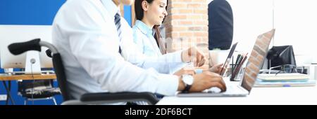 Man in wheelchair next to woman is sitting at desk and working Stock Photo