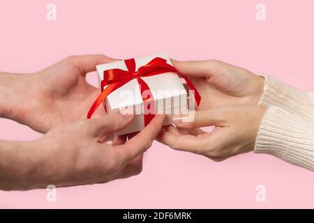 Man and Woman hands holding Gift box with red bow on pink background Stock Photo