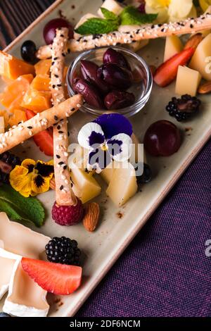 Cheese plate served with grapes and nuts. Assorted cheeses camembert, brie, parmesan blue cheese, goat with grapes, gressini sticks, cashews, honey an Stock Photo