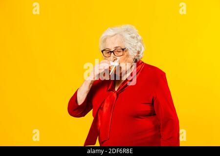 Studio portrait of a senior woman wearing red shirt drinking from a half pint of a beer against a yellow background Stock Photo