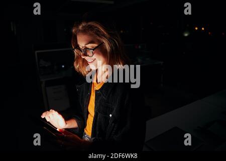 Portrait of a happy female executive standing near the desk using digital tablet in dark office room Stock Photo