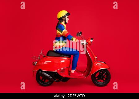 Photo portrait side view of woman riding scooter isolated on vivid red colored background Stock Photo