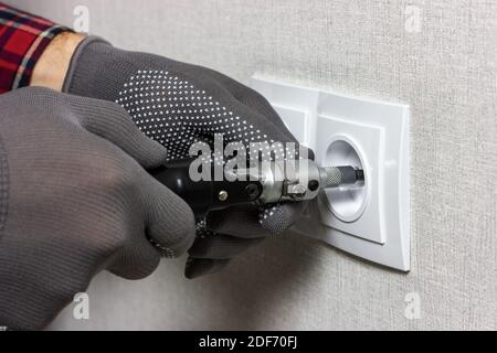 A foreman in gray work gloves installs an electrical outlet Stock Photo