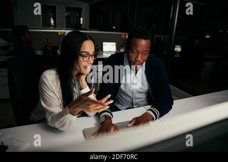 Multiethnic two business colleagues discussing new ideas sitting at the office table using laptop - colleagues working late at night trying to hit Stock Photo