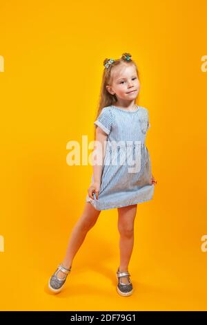 Adorable little model in trendy dress posing against bright yellow background Stock Photo
