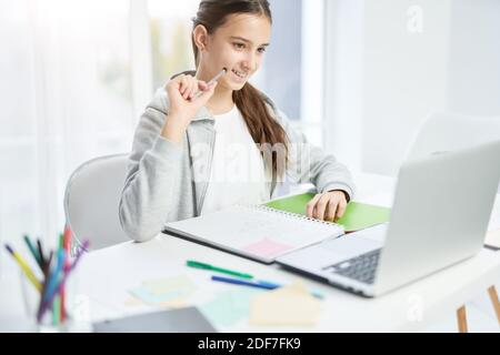 Cheerful latin teenage girl smiling, looking at the laptop screen while communicating with her teacher, having online lesson at home. Distance education, home schooling concept Stock Photo