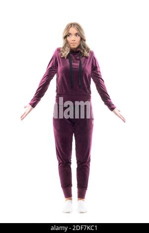 Confused cute young woman in home wear burgundy sweatsuit looking down and shrug shoulders. Full body length isolated on white background. Stock Photo