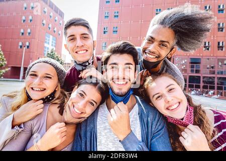 Multiracial friends taking selfie with opened face mask at college campus - Happy friendship concept with young students having fun together Stock Photo