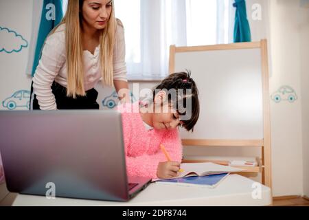 Schoolgirl with her mother at distance learning. Home schooling concept ...