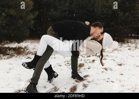 Young couple kissing in the winter forest. Snowing time. Lovers having fun on the snow. Love, relationship, winter holidays. Winter couple photo ideas Stock Photo