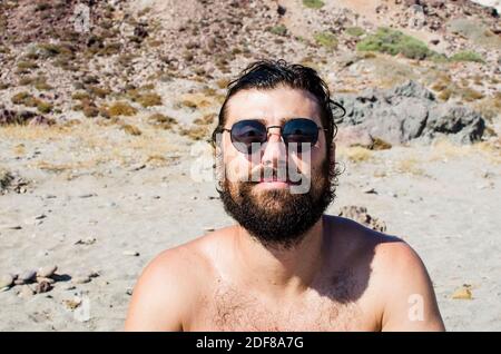 young man with wet hair after a bath on the beach wears sunglasses in casual style Stock Photo